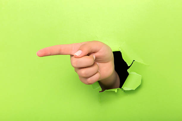 Female hand reaching through torn green paper sheet.hand showing one through the paper hole isolated on white background