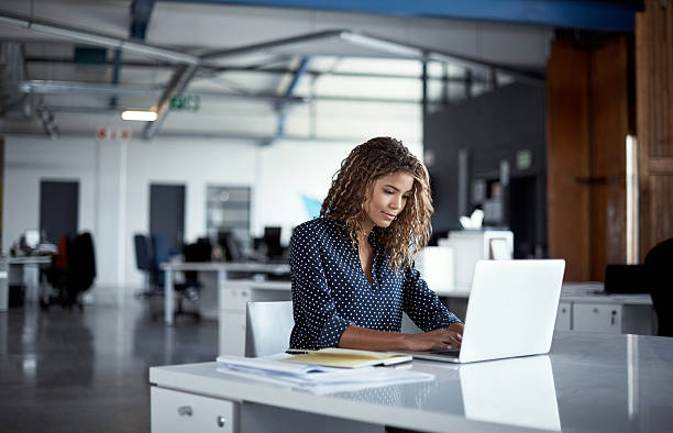 Merging business with the online world Cropped shot of a young businesswoman working on a laptop in a modern office using laptop stock pictures, royalty-free photos & images