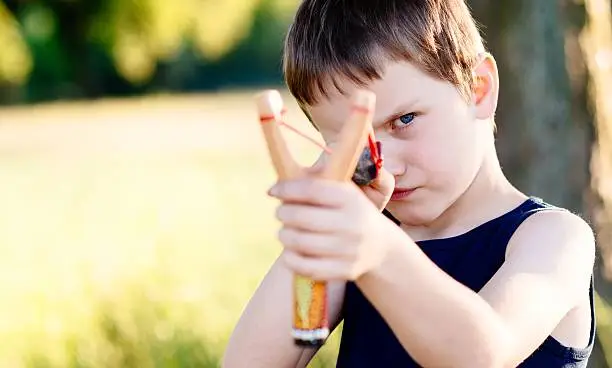 Little boy playing with slingshot at summer afternoon outdoors