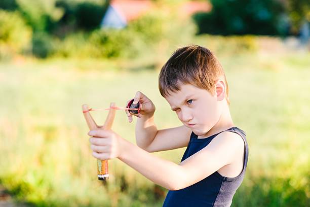 Little boy playing with slingshot Little boy playing with slingshot at summer afternoon outdoors baby gun stock pictures, royalty-free photos & images