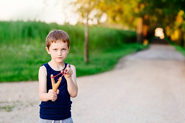 Little boy playing with slingshot Little boy playing with slingshot at summer afternoon outdoors baby gun stock pictures, royalty-free photos & images