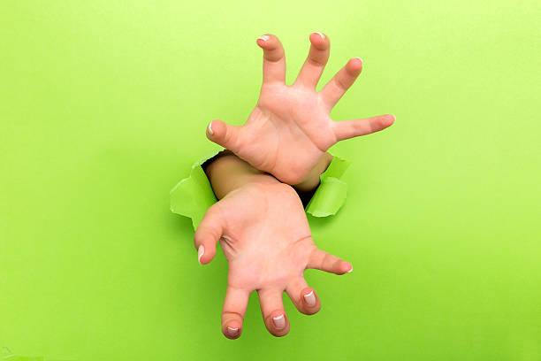 istock Female hand reaching through torn green paper sheet 598522606