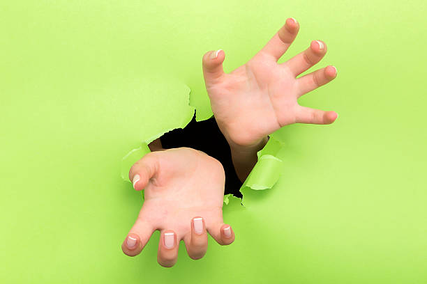 istock Female hand reaching through torn green paper sheet 598523078