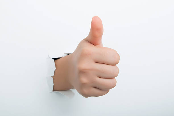 Thumbs up through the paper hole isolated on white background