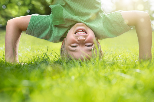 Young boy doing a headstand on the grass in the summer sunshine