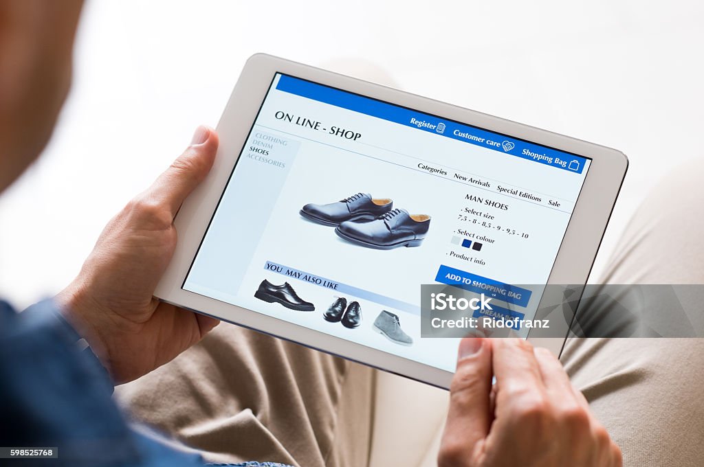 Man shopping online Young man looking at shoes online. Man looking at various shoes options over internet through digital tablet. Casual man makes online shopping at home with digital tablet. Internet Stock Photo