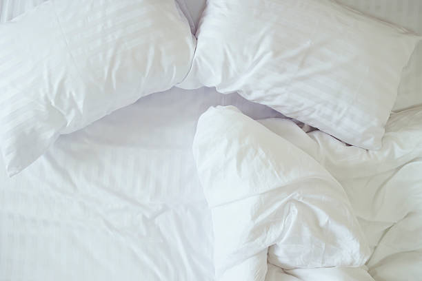 A close up shot of a neatly made bed with white sheets in a hotel room.