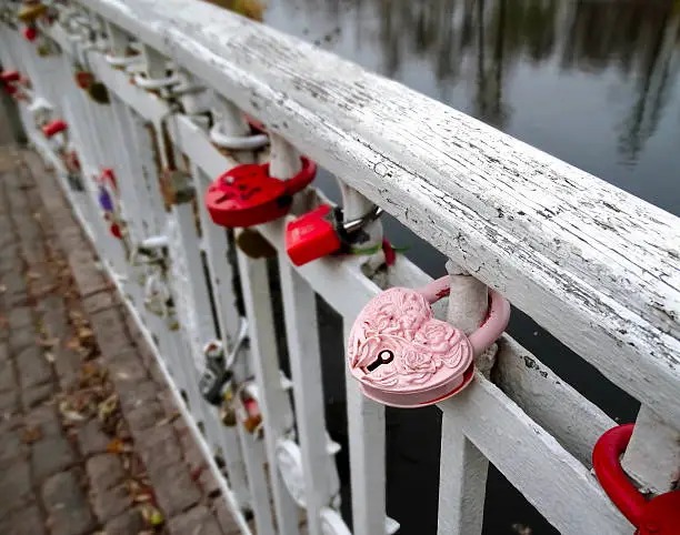 Romantic pink memory door-lock clipped on white handrail of a bridge in a park in November