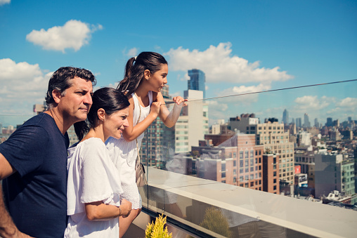 Family looking at New-York skyline on a bright summer day. Parents are in their forties, daughter is 10. Everybody is comfortably dressed with style. Very blue sky and white clouds in the background. Horizontal waist up outdoors shot with copy space. This was taken in New-York, USA.