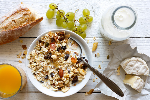 Healthy breakfast with muesli, grapes, cheese and juice on rustic white table from above.