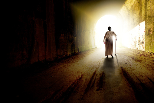 The figure of an elderly woman walking toward the light a the end of a tunnel.