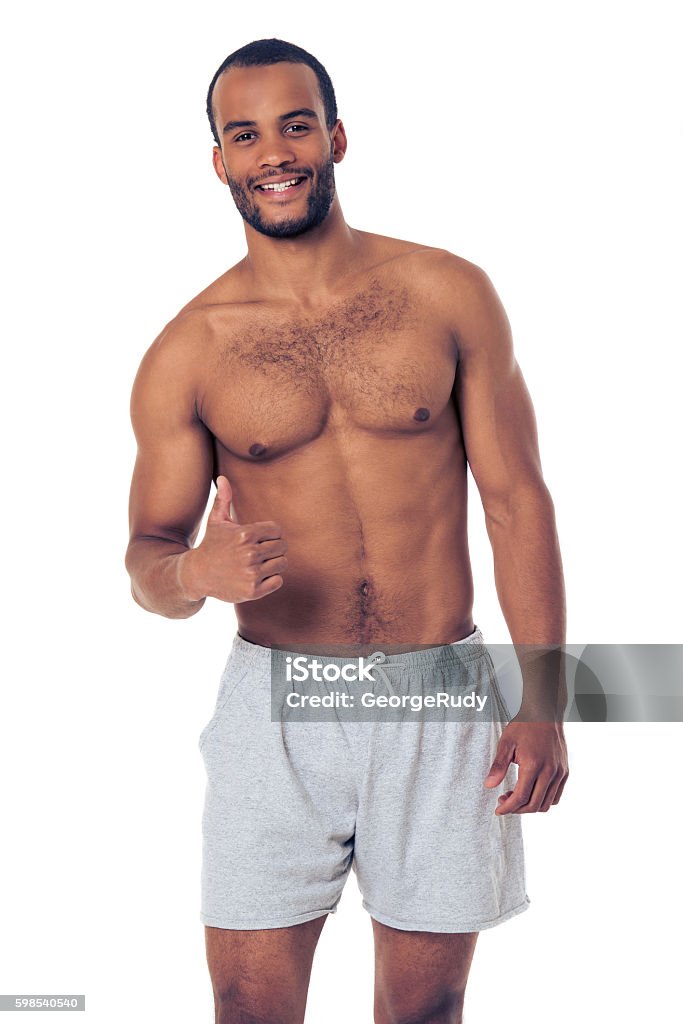 Handsome Afro American sportsman Handsome Afro American sportsman in gray shorts is showing Ok sign, looking at camera and smiling, isolated on white background Shirtless Stock Photo