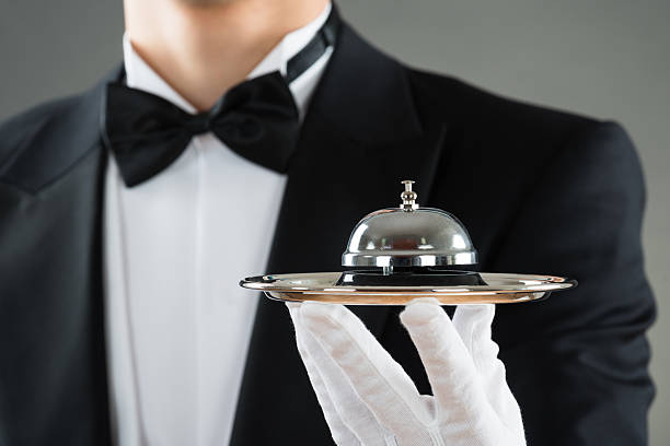 Midsection Of Waiter Holding Service Bell In Plate Midsection of waiter holding service bell in plate against gray background bellhop photos stock pictures, royalty-free photos & images