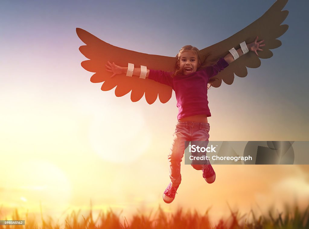 Kid with the wings of a bird Little girl plays outdoors. Child on the background of sunset sky. Kid with the wings of a bird dreams of flying. Aircraft Wing Stock Photo