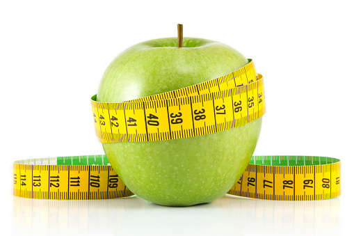 Diet and healthy eating concept. Green apple with green measuring tape on white background.