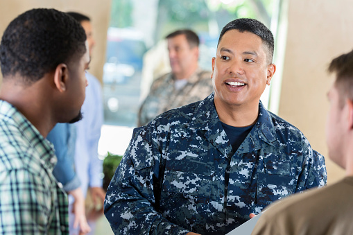 Mature adult Asian soldier is smiling while working in military recruitment office. He is talking to young adult about joining the armed forces.