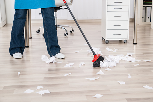 Close-up Of A Janitor Sweeping Torn Paper Pieces On Hardwood Floor