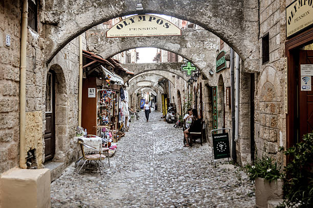Rhodes, Greece - June 22, 2016: Medieval streets in Old Town of Rhodes. Photo taken during a hot summer day and contains the occasional business and wandering tourist.