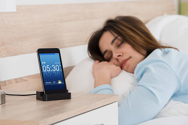 Woman Sleeping On Bed With Alarm On Mobile Phone Young Woman Sleeping On Bed With Alarm On Mobile Phone night table stock pictures, royalty-free photos & images