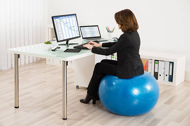 Businesswoman Sitting On Pilates Ball Working Young Businesswoman Sitting On Pilates Ball Working In Office fitness ball photos stock pictures, royalty-free photos & images