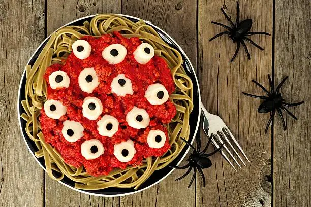 Halloween cheesy eyeball pasta with tomato meat sauce, above view on old wood with spiders