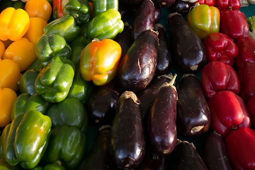 Eggplants and colored peppers arranged on a stand in a parisian market. France.