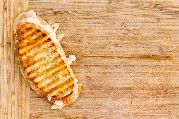 Appetizing grilled Italian panini bread cheese sandwich with melting cheese on a bamboo cutting board with copy space, overhead view