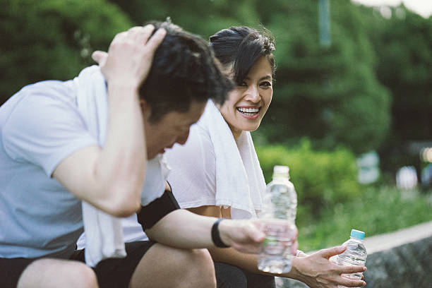 cheerful japanese couple relaxing after workout in a park - japanese culture asian ethnicity friendship computer imagens e fotografias de stock