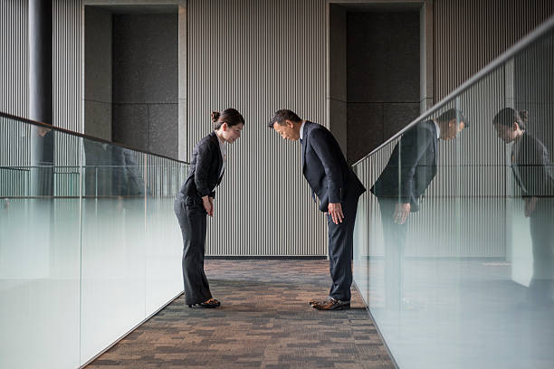 Two Japanese business people bowing towards each other Mature Japanese man and mid adult woman bowing in modern office interior bowing stock pictures, royalty-free photos & images
