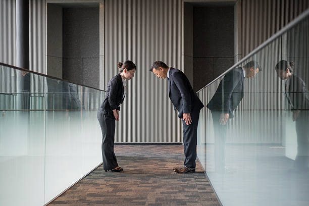 two japanese business people bowing towards each other - bowing imagens e fotografias de stock