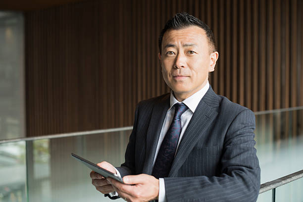 Portrait of mature Japanese businessman with tablet Male Japanese business manager holding digital tablet with serious expression japanese ethnicity stock pictures, royalty-free photos & images