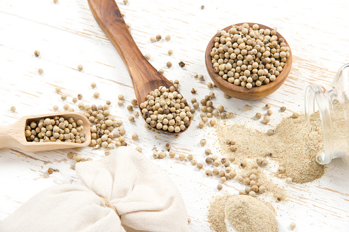 Photo of bowls full of white pepper seeds and powder on white wooden surface
