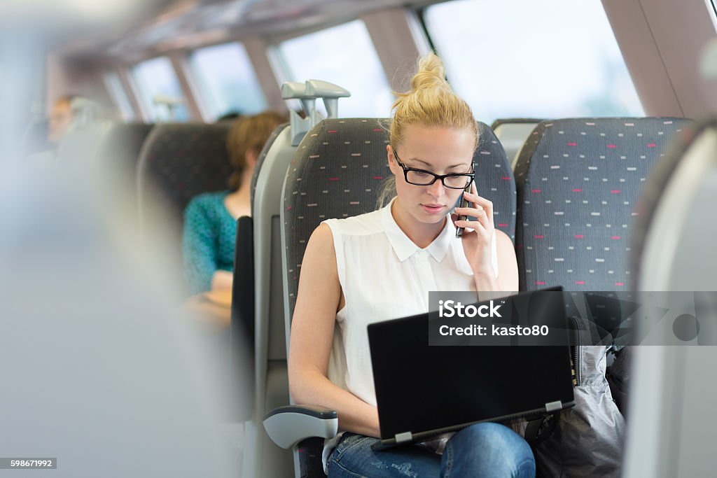 Business woman working while travelling by train. Businesswoman talking on cellphone and working on laptop while traveling by train. Business travel concept. Train - Vehicle Stock Photo