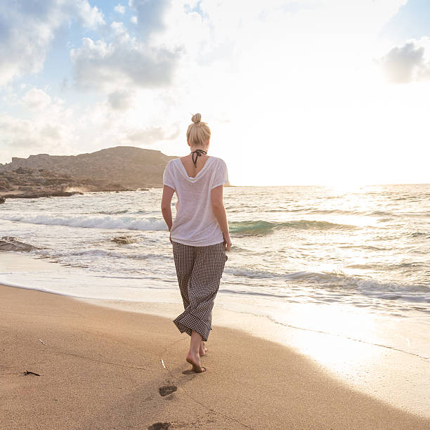 istock Woman walking on sand beach at golden hour 598672410