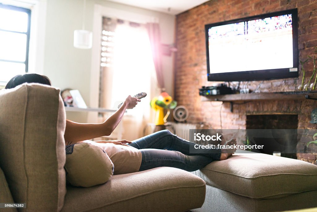 mujer relajándose en línea en el sofá leyendo algunos papeles - Foto de stock de Mirar la televisión libre de derechos