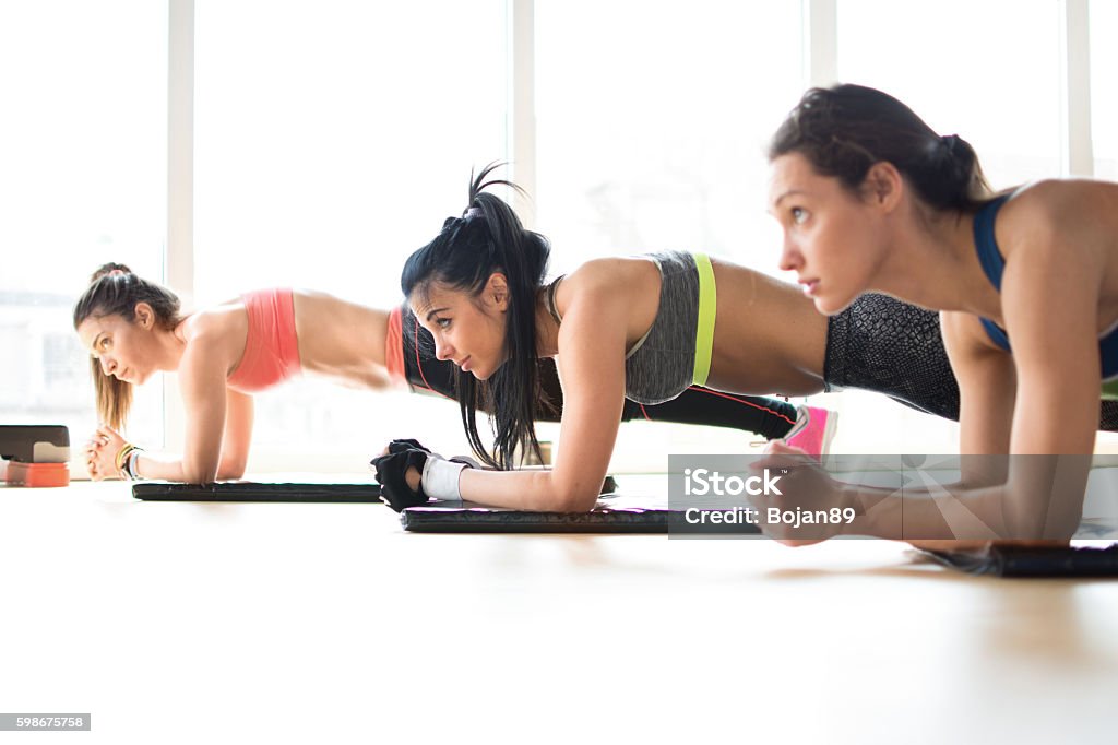 Three attractive sport girls doing plank exercise in fitness class. Three attractive sport girls doing plank exercise lying on yoga mat in fitness class. Exercising Stock Photo