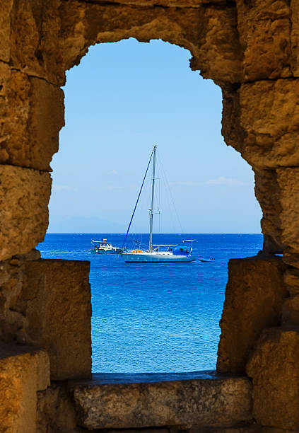 vista del barco y el mar desde las rendijas de las ventanas de las paredes de la fortaleza - scenics multi colored greece blue fotografías e imágenes de stock