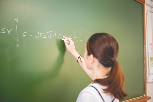 Pretty female student in uniform and with ponytail is doing math at the blackboard, Hong Kong, China, Asia. Copy space. Nikon D800, full frame, XXXL.
