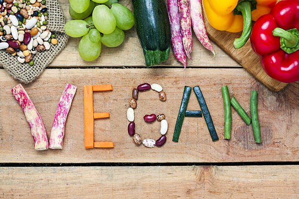 palabra vegana sobre fondo de madera y verdura - veganismo fotos fotografías e imágenes de stock