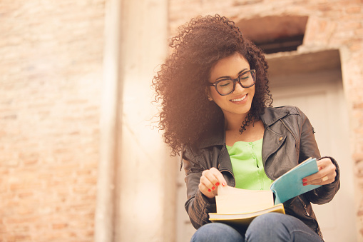 African american young woman smiling with books and glasses outdoors