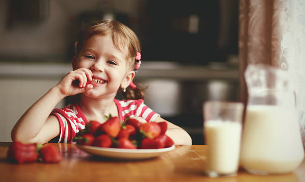 istock happy child girl eats strawberries in summer home kitchen 598711634