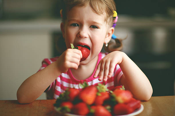 istock happy child girl eats strawberries in summer home kitchen 598711722