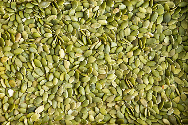 Background texture of green hulled pumpkin seeds Background texture of fresh healthy green de-husked pumpkin seeds a popular snack and salad ingredient rich in protein and nutrients zinc element stock pictures, royalty-free photos & images