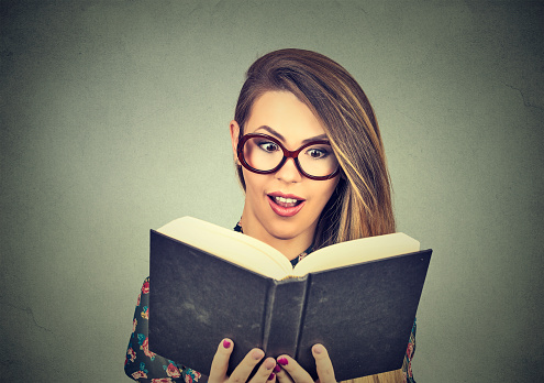 Portrait young woman in glasses reading big book isolated on gray wall background