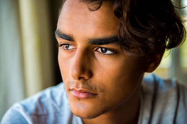 Portrait of young man looking away with blank expression. Young man watching outside from window and sunlights hit teenage boy's face. Image taken with NIKON D800 and developed from RAW format.