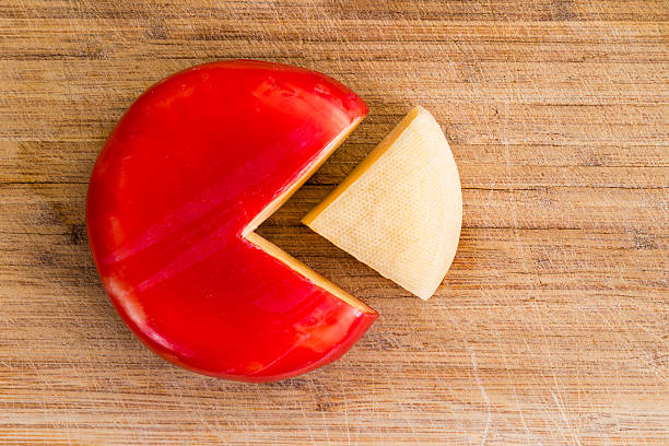 Wheel of fresh gouda cheese with a red rind Wheel of fresh gouda cheese with a red rind and a single wedge portion cut out, peeled and separated to the side on a wooden cutting board gouda cheese stock pictures, royalty-free photos & images