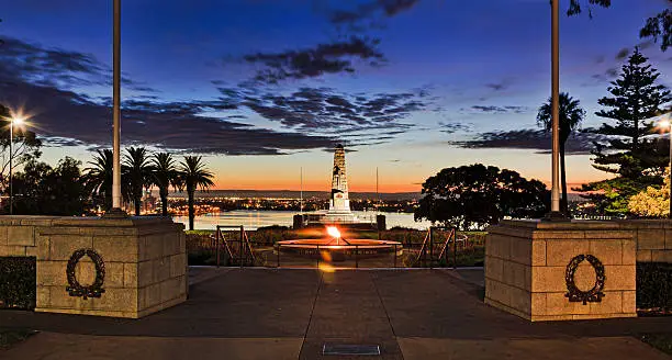 ANZAC memorial obelist in Kings Park of the city of Perth at sunrise during blue hour. Swan river flows in background behind stone column, rememberance fire and water pool.