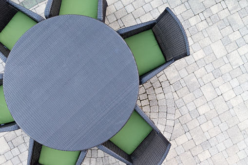 Six seater outdoor patio set with comfortable green cushions and a round dining table on a brick paved open-air patio with copyspace, overhead view