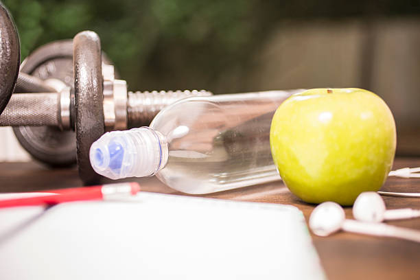 istock Fitness, exercise themed scene with weights, water, apple, journal. 598787388