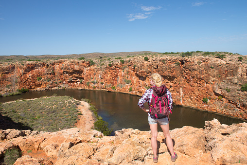 Blonde woman hiking in outback Australia, overlooking Yardie Creek river in Cape Range National Park, Exmouth, summer sunny blue sky, copy space.